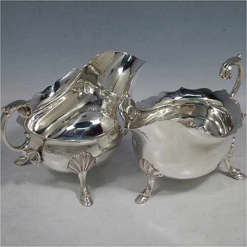 A handsome Antique Sterling Silver pair of sauce boats or gravy boats, having plain bellied bodies, with Chippendale borders, cast flying scroll handles with anthemion leaf thumb-pieces, and sitting on three cast hoof feet with shell shoulders. These elegant silver sauce boats were made by Walker & Hall of Sheffield in 1919. The dimensions of these fine hand-made antique silver gravy or sauce boats are length 15 cms (6 inches), width 9 cms (3.5 inches), height 9 cms (3.5 inches), and they weigh a total of approx. 390g (12.6 troy ounces).    