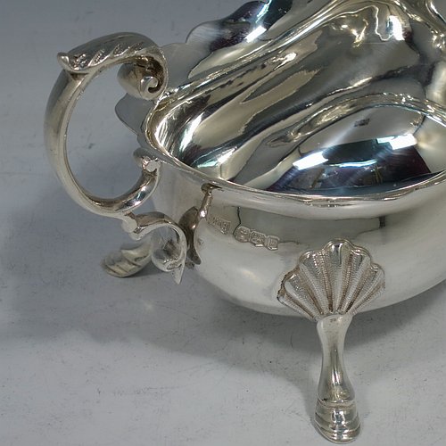 A handsome Antique Sterling Silver pair of sauce boats or gravy boats, having plain bellied bodies, with Chippendale borders, cast flying scroll handles with anthemion leaf thumb-pieces, and sitting on three cast hoof feet with shell shoulders. These elegant silver sauce boats were made by Walker & Hall of Sheffield in 1919. The dimensions of these fine hand-made antique silver gravy or sauce boats are length 15 cms (6 inches), width 9 cms (3.5 inches), height 9 cms (3.5 inches), and they weigh a total of approx. 390g (12.6 troy ounces).    