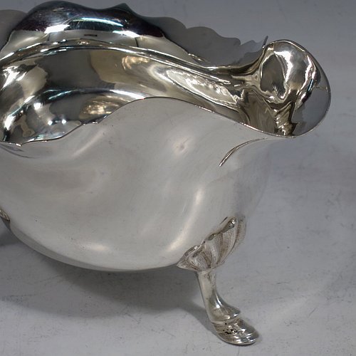 A handsome Antique Sterling Silver pair of sauce boats or gravy boats, having plain bellied bodies, with Chippendale borders, cast flying scroll handles with anthemion leaf thumb-pieces, and sitting on three cast hoof feet with shell shoulders. These elegant silver sauce boats were made by Walker & Hall of Sheffield in 1919. The dimensions of these fine hand-made antique silver gravy or sauce boats are length 15 cms (6 inches), width 9 cms (3.5 inches), height 9 cms (3.5 inches), and they weigh a total of approx. 390g (12.6 troy ounces).    