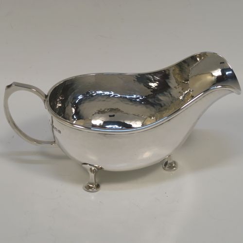 A Sterling Silver cream or sauce boat in an Arts and Crafts style, having a bellied body with hand-hammered or Planished decoration, a scroll side-handle, and sitting on three cast and panelled feet. This elegant silver sauce or cream boat was made by A. E. Jones of Birmingham in 1928. The dimensions of this fine hand-made silver cream or sauce boat are length 17 cms (6.75 inches), height 8 cms (3 inches), width 8.5 cms (3.25 inches), and it weighs approx. 162g (5.2 troy ounces).   