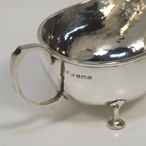 A Sterling Silver cream or sauce boat in an Arts and Crafts style, having a bellied body with hand-hammered or Planished decoration, a scroll side-handle, and sitting on three cast and panelled feet. This elegant silver sauce or cream boat was made by A. E. Jones of Birmingham in 1928. The dimensions of this fine hand-made silver cream or sauce boat are length 17 cms (6.75 inches), height 8 cms (3 inches), width 8.5 cms (3.25 inches), and it weighs approx. 162g (5.2 troy ounces).   