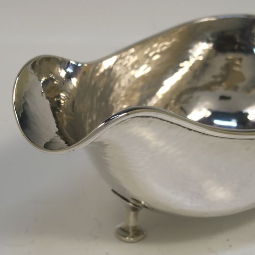 A Sterling Silver cream or sauce boat in an Arts and Crafts style, having a bellied body with hand-hammered or Planished decoration, a scroll side-handle, and sitting on three cast and panelled feet. This elegant silver sauce or cream boat was made by A. E. Jones of Birmingham in 1928. The dimensions of this fine hand-made silver cream or sauce boat are length 17 cms (6.75 inches), height 8 cms (3 inches), width 8.5 cms (3.25 inches), and it weighs approx. 162g (5.2 troy ounces).   