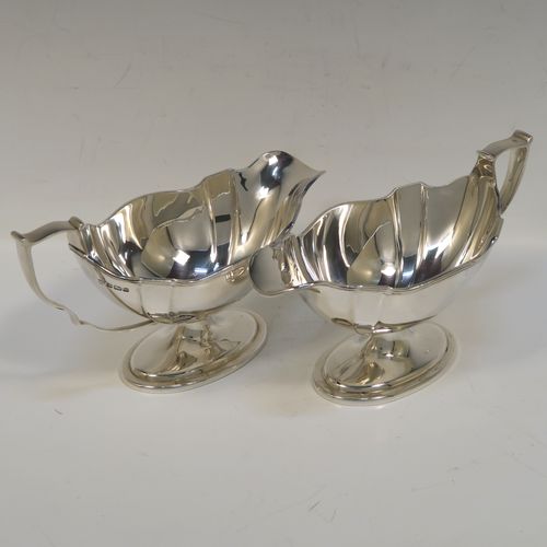 An elegant Antique Edwardian Sterling Silver pair of sauce boats, having plain shaped oval bellied bodies, with applied reeded borders, cast scroll side-handles, and sitting on pedestal feet. This handsome pair of silver sauce boats were made by Thomas Bradbury of Sheffield in 1910. The dimensions of this fine pair of hand-made antique sauce boats are length 18 cms (7 inches), height 10 cms (4 inches), width 8.5 cms (3.3 inches), and they weigh a total of approx. 497g (16 troy ounces).   