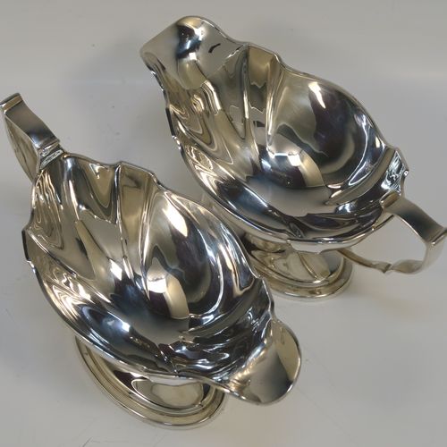 An elegant Antique Edwardian Sterling Silver pair of sauce boats, having plain shaped oval bellied bodies, with applied reeded borders, cast scroll side-handles, and sitting on pedestal feet. This handsome pair of silver sauce boats were made by Thomas Bradbury of Sheffield in 1910. The dimensions of this fine pair of hand-made antique sauce boats are length 18 cms (7 inches), height 10 cms (4 inches), width 8.5 cms (3.3 inches), and they weigh a total of approx. 497g (16 troy ounces).   