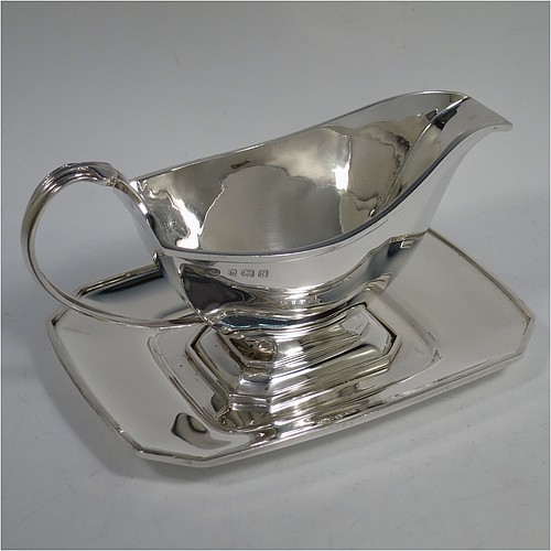 A Sterling Silver Art Deco style sauce or gravy boat on original stand, having a plain panelled body, with an applied reeded border, a scroll handle, sitting on an octagonal pedestal foot, and an original octagonal panelled drip stand. Made by the Adie Brothers of Birmingham in 1937. The dimensions of this fine hand-made Art Deco silver gravy or sauce boat and stand are length 18 cms (7 inches), width of stand 13 cms (5 inches), height 10 cms (4 inches), and it weighs a total of 430g (13.8 troy ounces). 