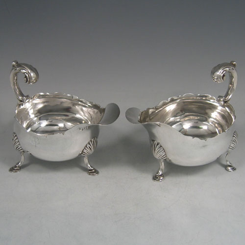 Antique Georgian sterling silver pair of sauce or gravy boats, having plain baluster bodies, chippendale borders, cast scoll handles, and sitting on three cast hoof feet with shell shoulders. Made by William Shaw II of London in 1765. The dimensions of these fine hand-made pair of antique silver sauce boats are length 16 cms (6.25 inches), width 10 cms (4 inches), height 11.5 cms (4.5 inches), and they weigh a total of 568g (18.3 troy ounces). Please note that these are crested.