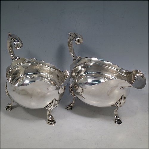 An Antique Georgian Sterling Silver pair of large George III sauce or gravy boats, having plain bellied bodies, with Chippendale borders, cast scroll handles, and sitting on three cast hoof feet with shell shoulders. Made by John Deacon (Possibly) of London in 1773/74. The dimensions of these fine hand-made antique silver sauce boats are length 18 cms (7 inches), width 10 cms (4 inches), height 13 cms (5 inches), and they weigh a total of 568g (18 troy ounces).    