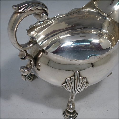 An Antique Georgian Sterling Silver pair of large George III sauce or gravy boats, having plain bellied bodies, with Chippendale borders, cast scroll handles, and sitting on three cast hoof feet with shell shoulders. Made by John Deacon (Possibly) of London in 1773/74. The dimensions of these fine hand-made antique silver sauce boats are length 18 cms (7 inches), width 10 cms (4 inches), height 13 cms (5 inches), and they weigh a total of 568g (18 troy ounces).    