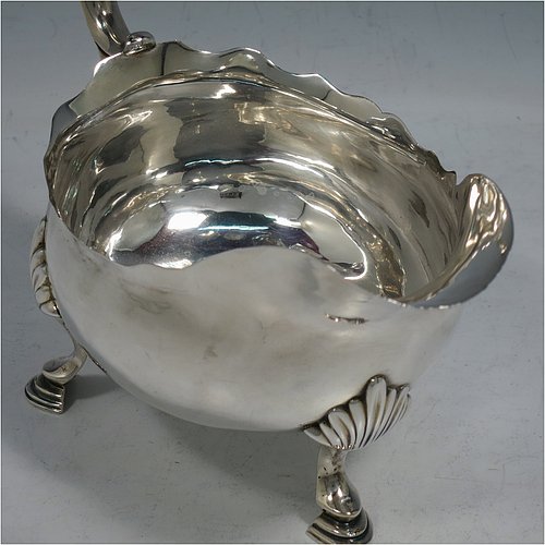 An Antique Georgian Sterling Silver pair of large George III sauce or gravy boats, having plain bellied bodies, with Chippendale borders, cast scroll handles, and sitting on three cast hoof feet with shell shoulders. Made by John Deacon (Possibly) of London in 1773/74. The dimensions of these fine hand-made antique silver sauce boats are length 18 cms (7 inches), width 10 cms (4 inches), height 13 cms (5 inches), and they weigh a total of 568g (18 troy ounces).    