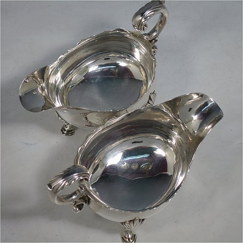 An Antique Georgian Sterling Silver pair of large George III sauce or gravy boats, having plain bellied bodies, with Chippendale borders, cast scroll handles, and sitting on three cast hoof feet with shell shoulders. Made by John Deacon (Possibly) of London in 1773/74. The dimensions of these fine hand-made antique silver sauce boats are length 18 cms (7 inches), width 10 cms (4 inches), height 13 cms (5 inches), and they weigh a total of 568g (18 troy ounces).    