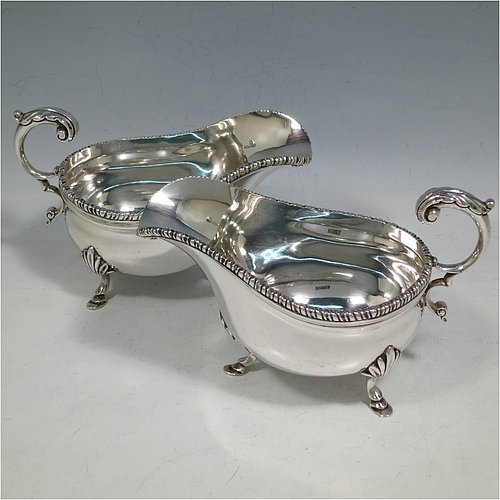 A Sterling Silver pair of sauce boats or gravy boats, having plain baluster bodies, with applied gadroon borders, cast flying scroll handles with anthemion leaf thumb-pieces, and sitting on three cast hoof feet with shell shoulders. Made by Mappin & Webb of London in 1925. The dimensions of these fine hand-made silver gravy or sauce boats are length 15 cms (6 inches), width 8.5 cms (3.3 inches), height 10 cms (4 inches), and they weigh a total of approx. 463g (15 troy ounces).   