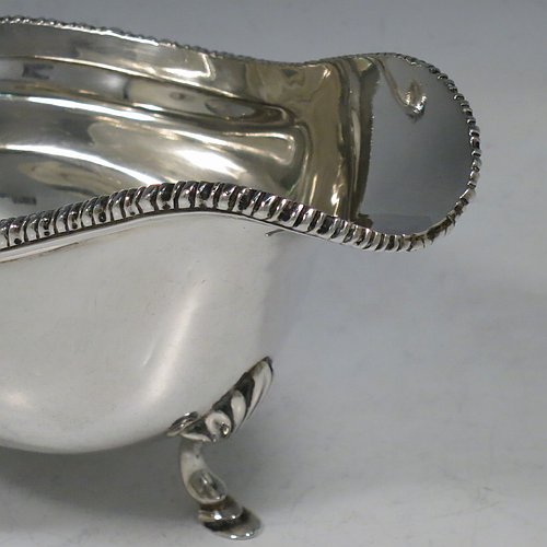 A Sterling Silver pair of sauce boats or gravy boats, having plain baluster bodies, with applied gadroon borders, cast flying scroll handles with anthemion leaf thumb-pieces, and sitting on three cast hoof feet with shell shoulders. Made by Mappin & Webb of London in 1925. The dimensions of these fine hand-made silver gravy or sauce boats are length 15 cms (6 inches), width 8.5 cms (3.3 inches), height 10 cms (4 inches), and they weigh a total of approx. 463g (15 troy ounces).   