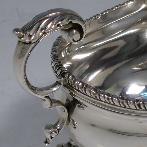 A Sterling Silver pair of sauce boats or gravy boats, having plain baluster bodies, with applied gadroon borders, cast flying scroll handles with anthemion leaf thumb-pieces, and sitting on three cast hoof feet with shell shoulders. Made by Mappin & Webb of London in 1925. The dimensions of these fine hand-made silver gravy or sauce boats are length 15 cms (6 inches), width 8.5 cms (3.3 inches), height 10 cms (4 inches), and they weigh a total of approx. 463g (15 troy ounces).   