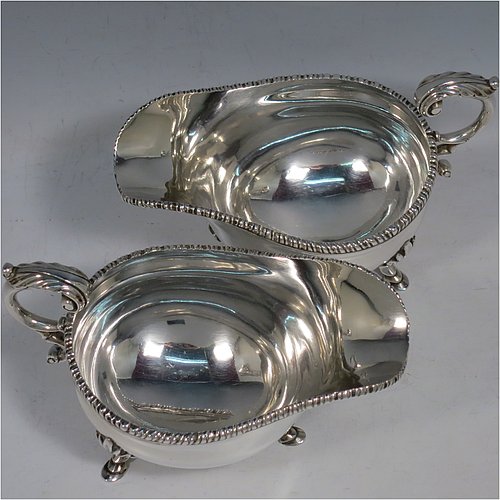 A Sterling Silver pair of sauce boats or gravy boats, having plain baluster bodies, with applied gadroon borders, cast flying scroll handles with anthemion leaf thumb-pieces, and sitting on three cast hoof feet with shell shoulders. Made by Mappin & Webb of London in 1925. The dimensions of these fine hand-made silver gravy or sauce boats are length 15 cms (6 inches), width 8.5 cms (3.3 inches), height 10 cms (4 inches), and they weigh a total of approx. 463g (15 troy ounces).   