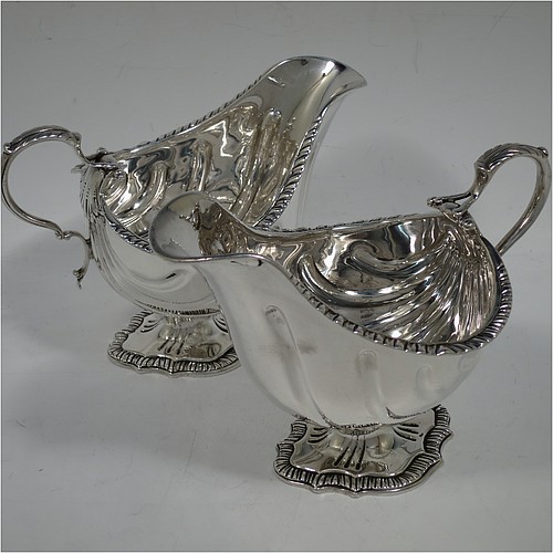 A very handsome Antique Edwardian Sterling Silver pair of sauce boats or gravy boats in a Georgian George II style, having bellied bodies with hand-chased swirl fluting, with applied gadroon borders, cast scroll handles with anthemion leaf tops, and sitting on shaped oval pedestal feet. Made by D & J Welby of London in 1904. The dimensions of these fine hand-made antique silver gravy or sauce boats are length 16.5 cms (6.5 inches), width 10 cms (4 inches), height 11.5 cms (4.5 inches), and they weigh a total of approx. 480g (15.5 troy ounces).   