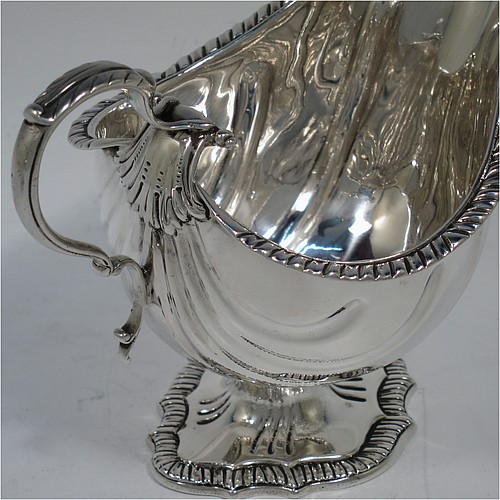 A very handsome Antique Edwardian Sterling Silver pair of sauce boats or gravy boats in a Georgian George II style, having bellied bodies with hand-chased swirl fluting, with applied gadroon borders, cast scroll handles with anthemion leaf tops, and sitting on shaped oval pedestal feet. Made by D & J Welby of London in 1904. The dimensions of these fine hand-made antique silver gravy or sauce boats are length 16.5 cms (6.5 inches), width 10 cms (4 inches), height 11.5 cms (4.5 inches), and they weigh a total of approx. 480g (15.5 troy ounces).   