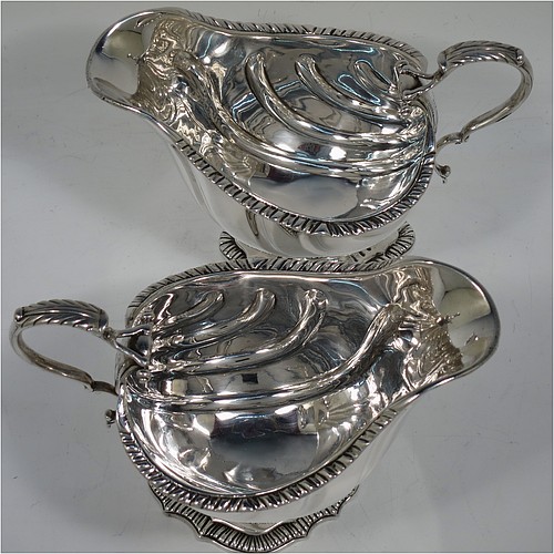 A very handsome Antique Edwardian Sterling Silver pair of sauce boats or gravy boats in a Georgian George II style, having bellied bodies with hand-chased swirl fluting, with applied gadroon borders, cast scroll handles with anthemion leaf tops, and sitting on shaped oval pedestal feet. Made by D & J Welby of London in 1904. The dimensions of these fine hand-made antique silver gravy or sauce boats are length 16.5 cms (6.5 inches), width 10 cms (4 inches), height 11.5 cms (4.5 inches), and they weigh a total of approx. 480g (15.5 troy ounces).   