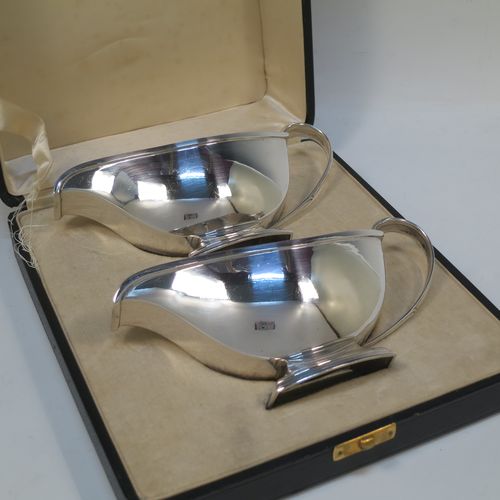 A stylish pair of Sterling Silver Art Deco sauce boats, having plain half-moon style bodies, scroll side-handles with thumb-pieces, square cross-section spouts, and sitting on a rectangular pedestal feet, all in their original cream satin and velvet-lined presentation box. Made by the Adie Brothers of Birmingham in 1937. The dimensions of this fine hand-made pair of silver sauce boats are length 16.5 cms (6.5 inches), height 7.5 cms (3 inches), width 7 cms (2.75 inches), and with a total weight of approx. 312g (10 troy ounces). Please note that the lids satin retaining strap is broken.