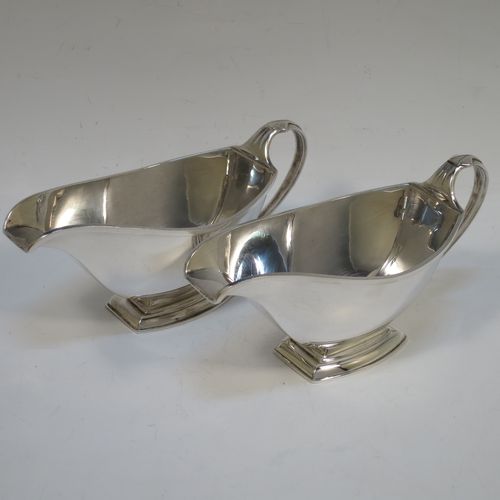 A stylish pair of Sterling Silver Art Deco sauce boats, having plain half-moon style bodies, scroll side-handles with thumb-pieces, square cross-section spouts, and sitting on a rectangular pedestal feet, all in their original cream satin and velvet-lined presentation box. Made by the Adie Brothers of Birmingham in 1937. The dimensions of this fine hand-made pair of silver sauce boats are length 16.5 cms (6.5 inches), height 7.5 cms (3 inches), width 7 cms (2.75 inches), and with a total weight of approx. 312g (10 troy ounces). Please note that the lids satin retaining strap is broken.