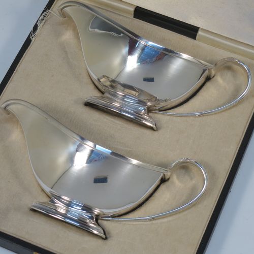 A stylish pair of Sterling Silver Art Deco sauce boats, having plain half-moon style bodies, scroll side-handles with thumb-pieces, square cross-section spouts, and sitting on a rectangular pedestal feet, all in their original cream satin and velvet-lined presentation box. Made by the Adie Brothers of Birmingham in 1937. The dimensions of this fine hand-made pair of silver sauce boats are length 16.5 cms (6.5 inches), height 7.5 cms (3 inches), width 7 cms (2.75 inches), and with a total weight of approx. 312g (10 troy ounces). Please note that the lids satin retaining strap is broken.