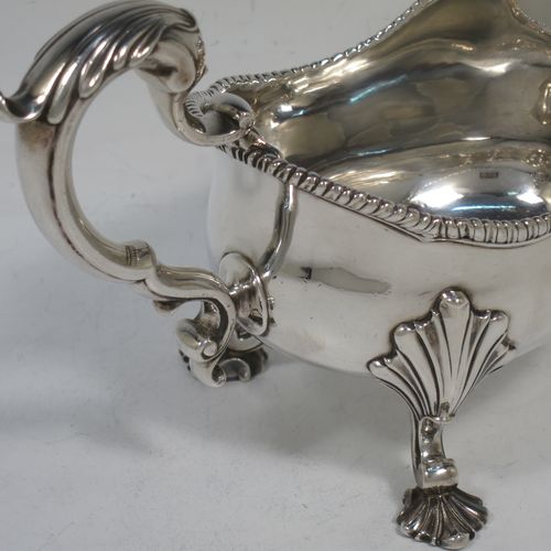 A handsome and heavy Antique Georgian Sterling Silver George III sauce or gravy boat, having a plain bellied body, with an applied shaped gadroon border, a cast scroll handle with anthemion leaf thumb-piece, and sitting on three cast shell feet with shell shoulders. Made in London in 1762. The dimensions of this fine hand-made antique silver sauce boat are length 19 cms (7.5 inches), width 9 cms (3.5 inches), height 12.5 cms (5 inches), and it weighs approx. 344g (11 troy ounces). Please note that this item is crested on one side.   