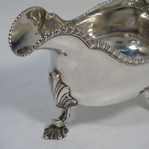 A handsome and heavy Antique Georgian Sterling Silver George III sauce or gravy boat, having a plain bellied body, with an applied shaped gadroon border, a cast scroll handle with anthemion leaf thumb-piece, and sitting on three cast shell feet with shell shoulders. Made in London in 1762. The dimensions of this fine hand-made antique silver sauce boat are length 19 cms (7.5 inches), width 9 cms (3.5 inches), height 12.5 cms (5 inches), and it weighs approx. 344g (11 troy ounces). Please note that this item is crested on one side.   