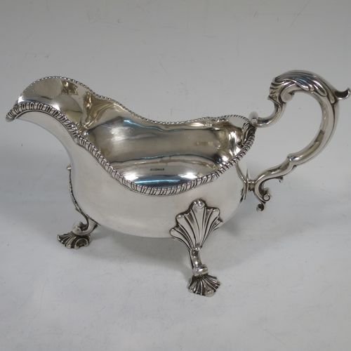 A handsome and heavy Antique Georgian Sterling Silver George III sauce or gravy boat, having a plain bellied body, with an applied shaped gadroon border, a cast scroll handle with anthemion leaf thumb-piece, and sitting on three cast shell feet with shell shoulders. Made in London in 1762. The dimensions of this fine hand-made antique silver sauce boat are length 19 cms (7.5 inches), width 9 cms (3.5 inches), height 12.5 cms (5 inches), and it weighs approx. 344g (11 troy ounces). Please note that this item is crested on one side.   