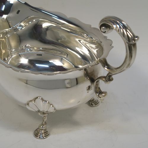 A handsome Sterling Silver pair of sauce boats or gravy boats, having plain bellied bodies, with Chippendale borders, cast flying scroll handles with anthemion leaf thumb-pieces, and sitting on three cast hoof feet with shell shoulders. These elegant silver sauce boats were made by Mappin and Webb of Sheffield in 1976. The dimensions of these fine hand-made silver gravy or sauce boats are length 19 cms (7.5 inches), width 11 cms (4.3 inches), height 12 cms (4.75 inches), and they weigh a total of approx. 534g (17.2 troy ounces).  