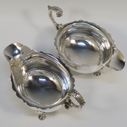 A handsome Sterling Silver pair of sauce boats or gravy boats, having plain bellied bodies, with Chippendale borders, cast flying scroll handles with anthemion leaf thumb-pieces, and sitting on three cast hoof feet with shell shoulders. These elegant silver sauce boats were made by Mappin and Webb of Sheffield in 1976. The dimensions of these fine hand-made silver gravy or sauce boats are length 19 cms (7.5 inches), width 11 cms (4.3 inches), height 12 cms (4.75 inches), and they weigh a total of approx. 534g (17.2 troy ounces).  