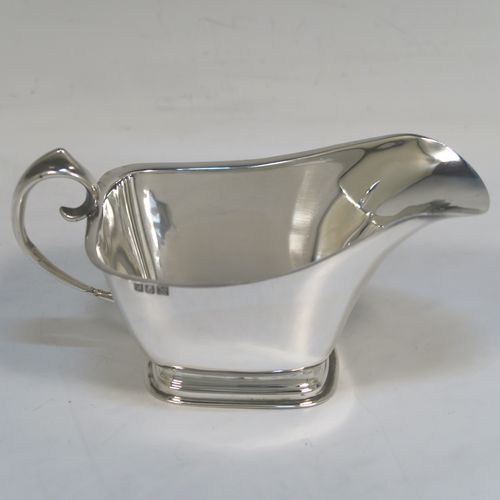 A stylish pair of Sterling Silver Irish cream or sauce boats in a Modernistic style, having plain bodies with tapering sides, scroll side-handles with thumb-pieces, and sitting on rectangular pedestal feet. These elegant silver sauce or cream boats were hallmarked for Dublin in 1965. The dimensions of this fine hand-made pair of silver cream or sauce boats are length 14 cms (5.5 inches), height 7.5 cms (3 inches), width 7 cms (2.75 inches), and with a total weight of approx. 223g (7.2 troy ounces).   