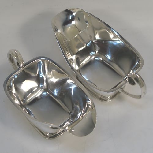 A stylish pair of Sterling Silver Irish cream or sauce boats in a Modernistic style, having plain bodies with tapering sides, scroll side-handles with thumb-pieces, and sitting on rectangular pedestal feet. These elegant silver sauce or cream boats were hallmarked for Dublin in 1965. The dimensions of this fine hand-made pair of silver cream or sauce boats are length 14 cms (5.5 inches), height 7.5 cms (3 inches), width 7 cms (2.75 inches), and with a total weight of approx. 223g (7.2 troy ounces).   