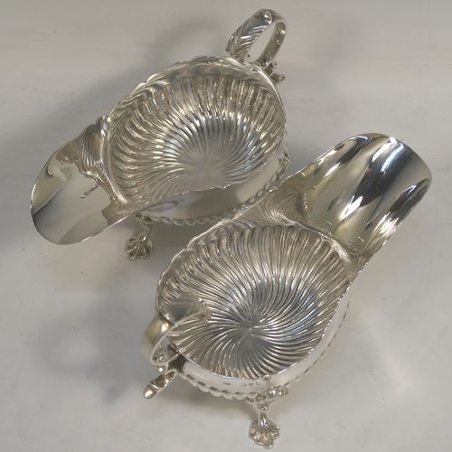 A very pretty pair of Antique Victorian Sterling Silver sauce or gravy boats, having hand-chased half-fluted decoration, with Chippendale top borders, cast scroll handles, and sitting on three cast floral feet. These beautiful antique silver sauce boats were made by John Henry Rawlings of London in 1890. The dimensions of these fine hand-made silver gravy or sauce boats are length 16.5 cms (6.5 inches), width 9 cms (3.5 inches), height 10 cms (4 inches), and they weigh a total of approx. 462g (15 troy ounces).   