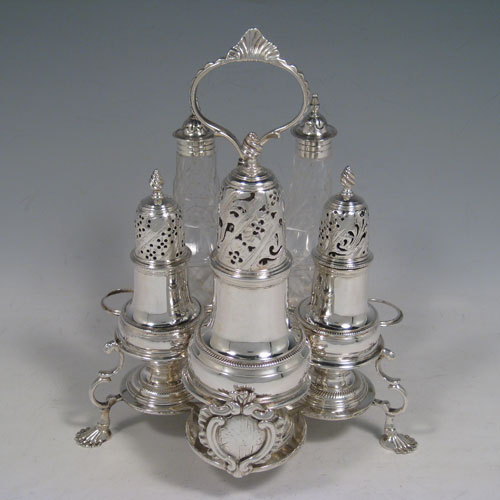 Antique Georgian sterling silver and hand-cut crystal five-bottle Warwick style cruet set, having a stand with scroll work holders, a cast and twisted loop handle, a cast applied cartouche and sitting on four cast shell feet. With two smaller baluster style pepper pots, a larger caster, and two crystal shakers with silver tops. Made by Jabez Daniel and James Mince of London in 1767. The dimensions of this fine hand-made silver cruet set are width of stand 19 cms (7.5 inches), height of stand 23 cms (9 inches), and weight of silver approx. 770g (24.8 troy ounces). Please note that the silver tops on the crystal bottles are unmarked, and the stand is crested.   