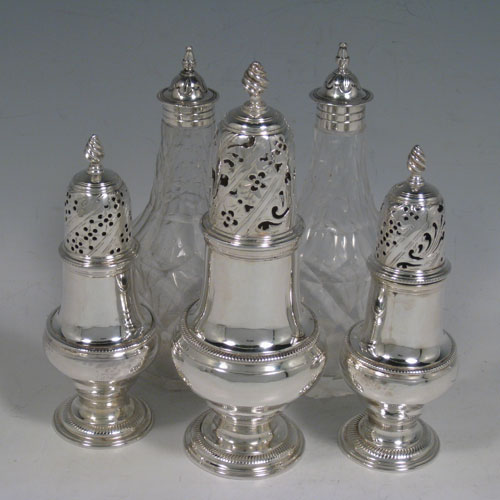 Antique Georgian sterling silver and hand-cut crystal five-bottle Warwick style cruet set, having a stand with scroll work holders, a cast and twisted loop handle, a cast applied cartouche and sitting on four cast shell feet. With two smaller baluster style pepper pots, a larger caster, and two crystal shakers with silver tops. Made by Jabez Daniel and James Mince of London in 1767. The dimensions of this fine hand-made silver cruet set are width of stand 19 cms (7.5 inches), height of stand 23 cms (9 inches), and weight of silver approx. 770g (24.8 troy ounces). Please note that the silver tops on the crystal bottles are unmarked, and the stand is crested.   