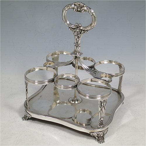 An Antique Georgian Sterling Silver large table cruet set, having a Regency style rectangular  stand with an applied gadroon border, with ring handle and a frame for six hand-cut crystal cruet bottles with original stoppers and silver mounts, all sitting on a base with four cast lions paw  feet. Made by William Bateman I of London in 1825. The dimensions of this fine antique silver cruet set are height 20 cms (8 inches), length 15 cms (6 inches), and width 13 cms (5 inches). Please note that the base has a wooden insert underneath.   