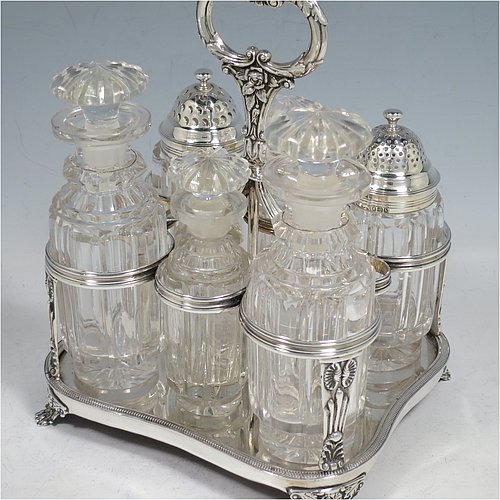 An Antique Georgian Sterling Silver large table cruet set, having a Regency style rectangular  stand with an applied gadroon border, with ring handle and a frame for six hand-cut crystal cruet bottles with original stoppers and silver mounts, all sitting on a base with four cast lions paw  feet. Made by William Bateman I of London in 1825. The dimensions of this fine antique silver cruet set are height 20 cms (8 inches), length 15 cms (6 inches), and width 13 cms (5 inches). Please note that the base has a wooden insert underneath.   