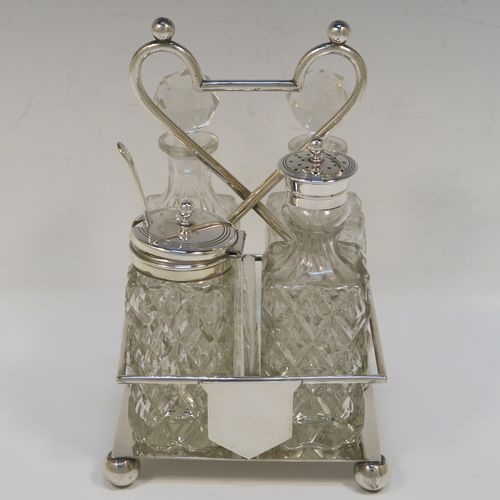 A handsome Antique Victorian Silver Plated and hand-cut crystal cruet set, having four crystal bottles with original stoppers and silver mounts, consisting of an oil and vinegar, a mustard pot spoon, and a pepper shaker, all sitting in a square galleried frame with a wire-work looped handle, and sitting on four cast ball feet. This original antique silver-plated cruet set was ca. 1870. The dimensions of this fine hand-made antique silver-plated cruet set are height of frame 19 cms (7.5 inches), and 11.5 cms (4.5 inches) square.   