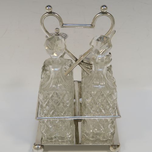 A handsome Antique Victorian Silver Plated and hand-cut crystal cruet set, having four crystal bottles with original stoppers and silver mounts, consisting of an oil and vinegar, a mustard pot spoon, and a pepper shaker, all sitting in a square galleried frame with a wire-work looped handle, and sitting on four cast ball feet. This original antique silver-plated cruet set was ca. 1870. The dimensions of this fine hand-made antique silver-plated cruet set are height of frame 19 cms (7.5 inches), and 11.5 cms (4.5 inches) square.   