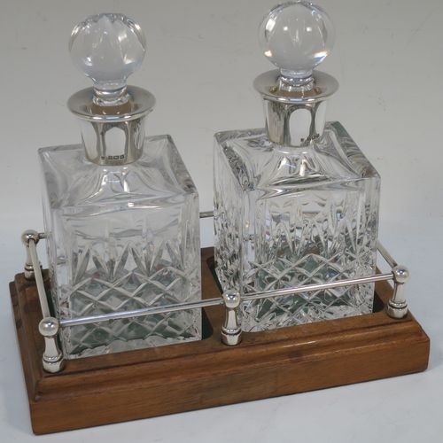 A very handsome pair of small Sterling Silver and hand-cut crystal decanters sitting in a galleried wood base, having square cross-section bodies with silver collars and original stoppers, all sitting in a silver galleried wooden base with green felt interiors. Made by Charles S. Green and Co. Ltd., of Birmingham in 1986. The dimensions of this fine pair of silver and crystal decanters (including base) are height 17 cms (6.75 inches), length 19 cms (7.5 inches), and width 10 cms (4 inches).  