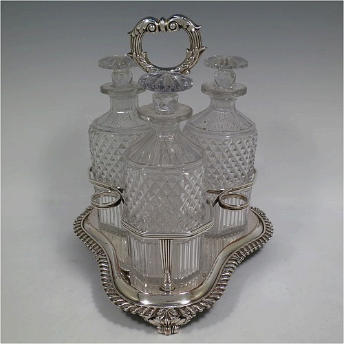 A very handsome Antique Georgian Old Sheffield plated decanter stand, having three hand-cut crystal decanters with original stoppers, sitting inside a carrying frame with a cast anthemion leaf loop handle attached to a hand-chased reeded gallery, which in-turn is attached to a base with shell and gadroon border, and all sitting on three cast scroll feet. Made by Matthew Boulton of Birmingham in ca. 1810. The dimensions of this fine hand-made Old Sheffield plated decanter stand are height 28 cms (11 inches), and width at base 25.5 cms (10 inches).   