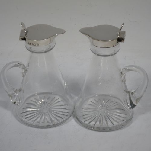 A very handsome pair of Sterling Silver and crystal whisky toddies or noggins, having round based hand-cut crystal bodies with tapering sides and loop handles, mounted with silver collars and hinged flat lids with thumb-pieces, all sitting on flat star-cut bases. Made by Hukin and Heath of Birmingham in 1923. The dimensions of this fine hand-made pair of silver and crystal noggins or toddies are height 11 cms (4.25 inches), and diameter at bases 6.5 cms (2.5 inches).    