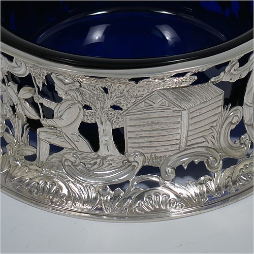 An Antique Victorian Sterling Silver large table dish ring in an Irish style, having a hand-pierced and chased body decorated with pastoral scenes, figures, animals, a vacant oval cartouche, and a blue-glass liner. Made by D. and J. Welby of London in 1894. The dimensions of this fine hand-made antique silver dish ring are height 7.5 cms (3 inches), diameter at base 19 cms (7.5 inches), and it weighs approx. 351g (11.3 troy ounces).    