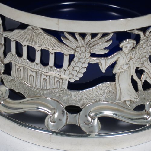 An Antique Edwardian Sterling Silver large table dish ring in an Irish style, having a hand-pierced and chased body decorated with pastoral scenes, figures, and animals, and a blue-glass liner. Made by Israel Sigmund Greenberg of Birmingham in 1904. The dimensions of this fine hand-made antique silver dish ring are height 10 cms (4 inches), diameter at base 20 cms (8 inches), and it weighs approx. 387g (12.5 troy ounces).    