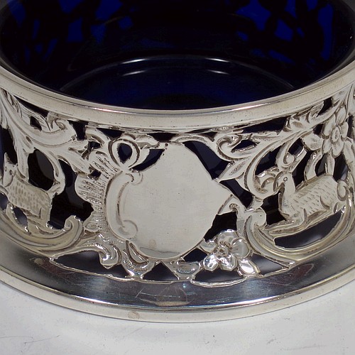 A handsome Antique Victorian Sterling silver miniature dish ring, in an Irish style, having a hand-pierced and chased body with with pastoral scenes, figures, animals, a vacant oval cartouche, and a blue-glass liner. Made by John and Frank Pairpoint of London in 1901. The dimensions of this fine hand-made antique miniature silver dish ring are height 5 cms (2 inches), diameter at base 11 cms (4.3 inches), and it weighs approx. 108g (3.5 troy ounces).    