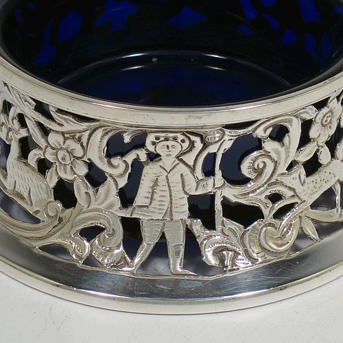 A handsome Antique Victorian Sterling silver miniature dish ring, in an Irish style, having a hand-pierced and chased body with with pastoral scenes, figures, animals, a vacant oval cartouche, and a blue-glass liner. Made by John and Frank Pairpoint of London in 1901. The dimensions of this fine hand-made antique miniature silver dish ring are height 5 cms (2 inches), diameter at base 11 cms (4.3 inches), and it weighs approx. 108g (3.5 troy ounces).    