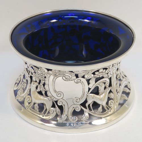 A very beautiful Irish Antique Sterling Silver large table dish ring, having a hand-pierced and chased body decorated with scrolls, flowers, and animals, a single vacant cartouche, and a blue-glass liner. This elegant silver potato or dish ring was made by West and Son of Dublin in 1917. The dimensions of this fine hand-made antique silver dish ring are height 10 cms (4 inches), diameter at base 18.5 cms (7.25 inches), and it weighs approx. 326g (10.5 troy ounces).   