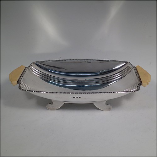 A Sterling Silver Art Deco dish, having a rectangular body with hand-chased reeded decoration, an applied floral border together with two hand-cut stepped bone handles, and sitting on four flanged feet. Made by George Bryan and Co., of Birmingham in 1938. The dimensions of this fine hand-made Art Deco silver serving dish are length 32 cms (12.5 inches), width 16.5 cms (6.5 inches), height 6.5 cms (2.5 inches), and it weighs approx. 620g (20 troy ounces).