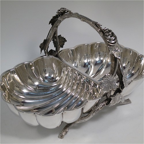 An Antique Victorian Silver Plated very unusual double shell bread roll or biscuit dish, having two connected side dishes with hand-chased shell style decoration, with a central cast vine-leaf and tendril handle, and sitting on four cast branch-like feet. Made by Mappin and Webb in their Princes Plate in ca. 1880. The dimensions of this fine hand-made antique silver-plated biscuit or bread roll dish are length 30 cms (11.75 inches), width 20 cms (8 inches), and height 17 cms (6.75 inches).    