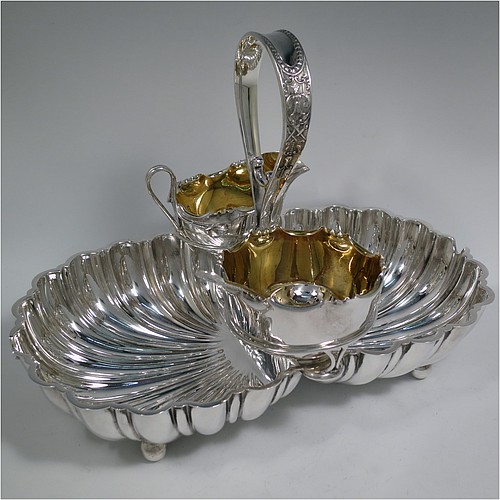 An Antique Victorian Silver-Plated strawberry dish, having two melon-fluted fixed shell dishes, a removable sugar bowl and cream jug both with gold-gilt interiors, an original sugar sifting ladle, and all sitting in a frame with loop handle and four ball feet. Made by James Dixon and Sons of Sheffield in ca. 1880. The dimensions of this fine hand-made antique silver-plated double strawberry dish are length 32 cms (12.5 inches), width 20 cms (8 inches), and height 22 cms (8.75 inches).   