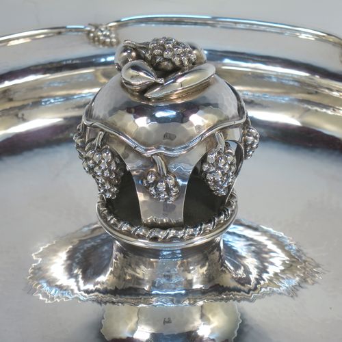 A very elegant and unusual Sterling Silver Arts and Crafts style large table fruit dish, having a round hand-hammered body, a central handle with cast grape and fruit decoration, and an applied grape border. Made by A. E. Jones of Birmingham in 1936. The dimensions of this fine hand-made silver fruit dish are diameter 31 cms (12.25 inches), height 10 cms (4 inches), and it weighs approx. 1,080g (34.8 troy ounces).  